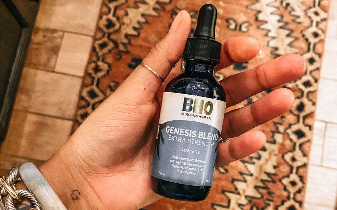 A woman's hand gracefully holds a bottle of Genesis Blend Full Spectrum Extra Strength CBD Oil, poised to administer a dose.