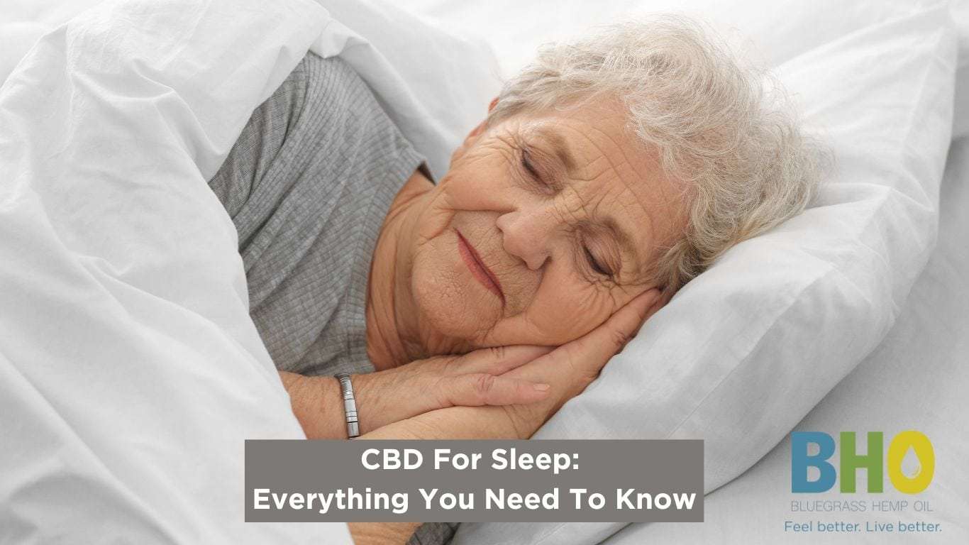 An older lady peacefully asleep on a soft pillow, with the CBD product Genesis Blend CBD for Sleep prominently displayed on the nightstand beside her.