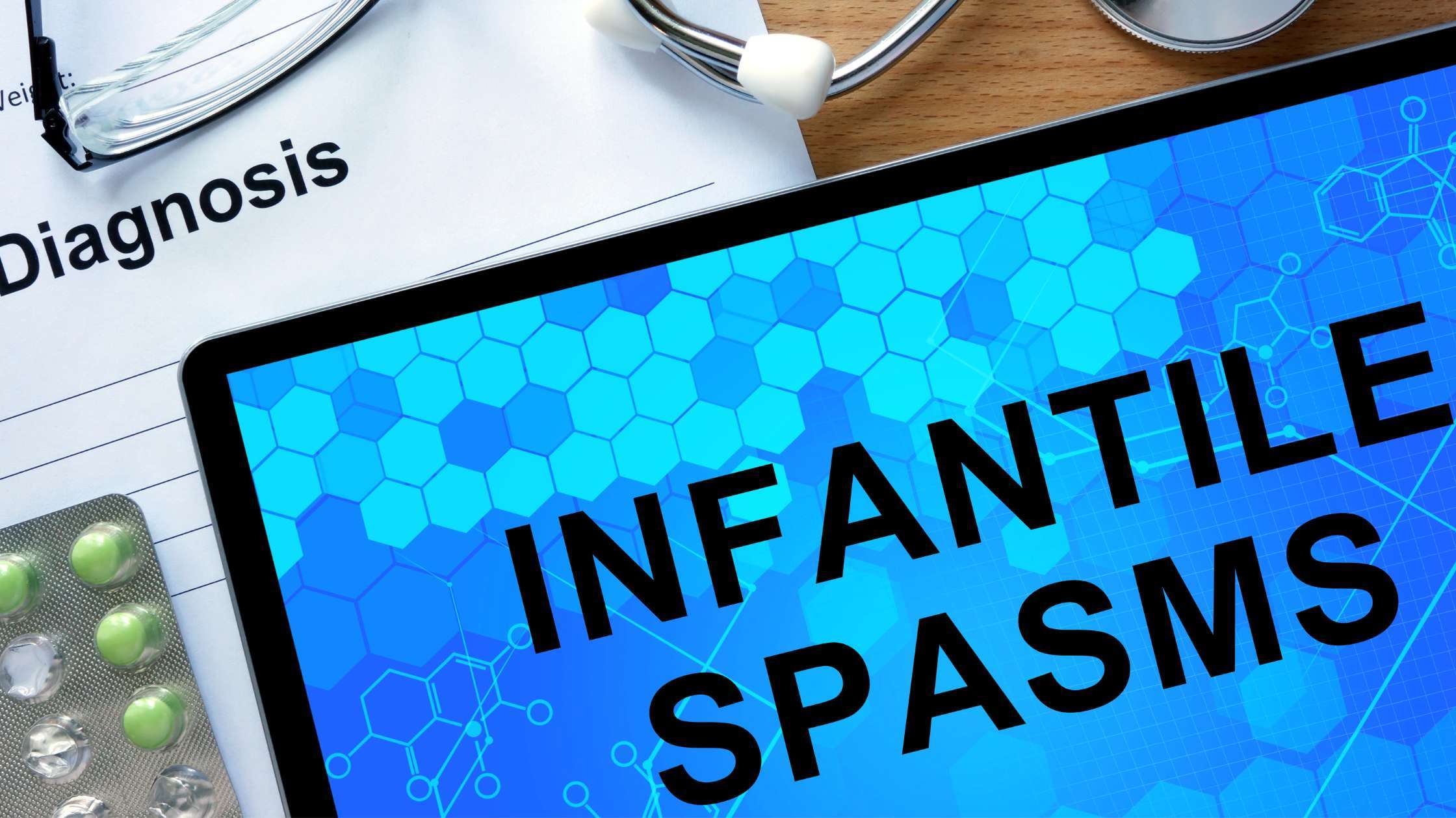 Laptop screen displaying the words 'Infantile Spasms' with a prescription pad in the background.