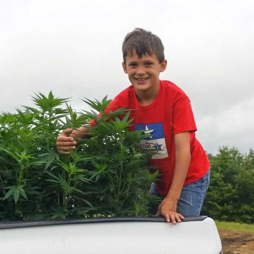 Colten Polyniak sitting in the back of a pickup truck surrounded by CBD hemp plants before heading to the field for planting.